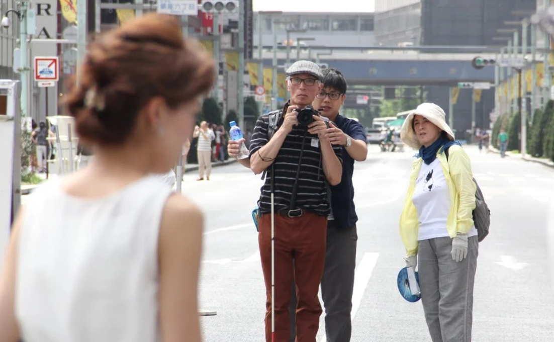 写真家尾崎さんに聞く、世界の見方と伝え方トップ写真。白杖を持ち、カメラを構える尾崎さん